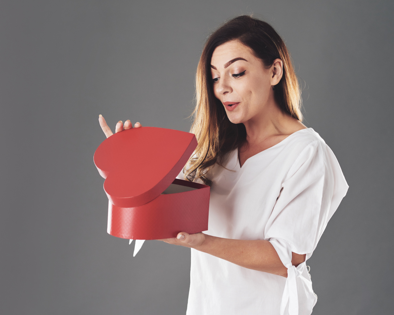 Любопытная девушка смотрит в красную коробку в форме сердца