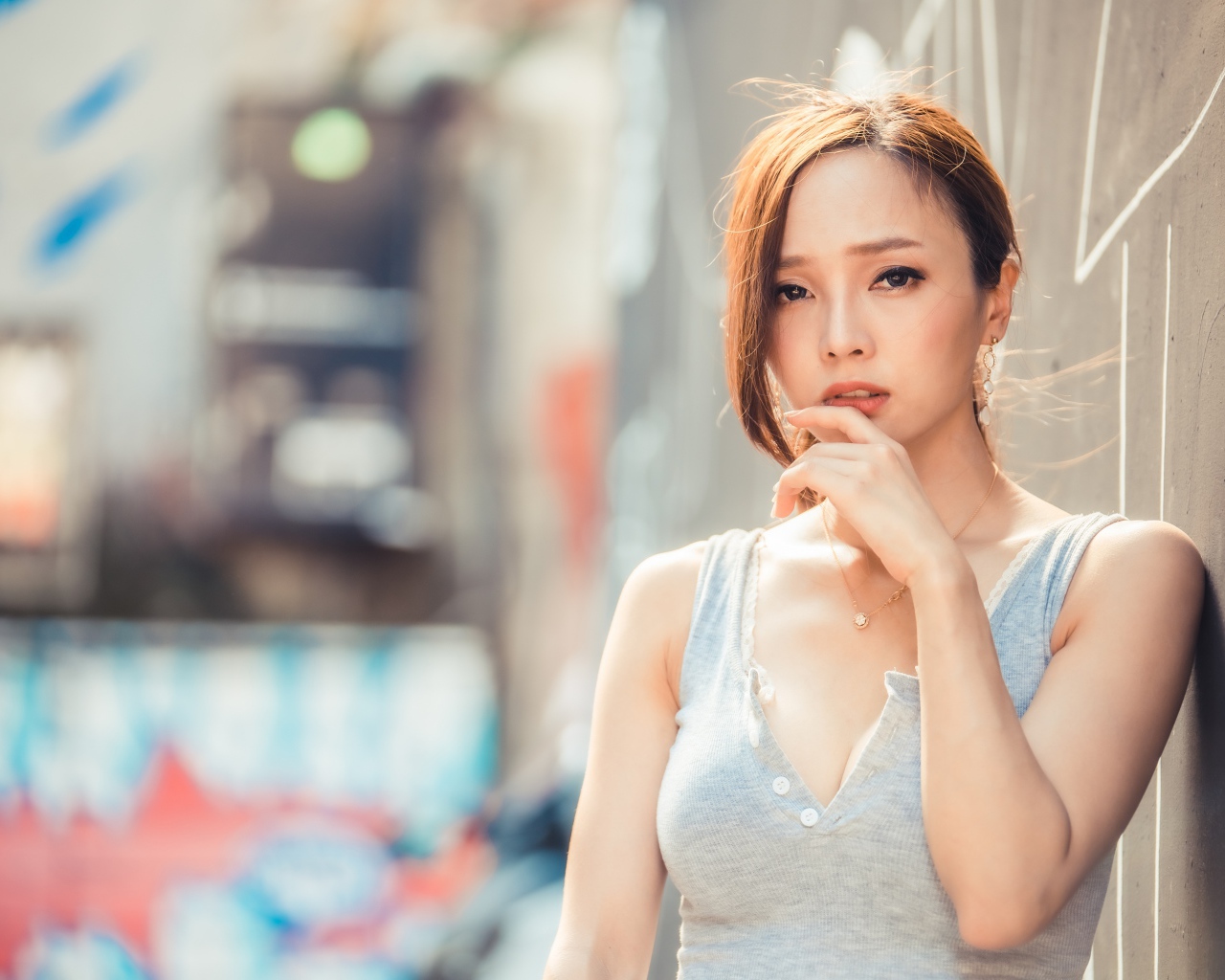 Милая девушка азиатка  с рукой у лица стоит у стены 
