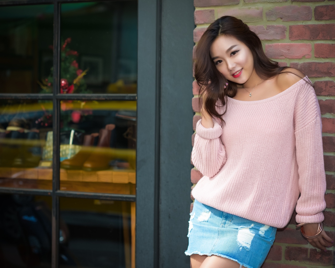 Милая азиатка в розовом свитере стоит у стены 