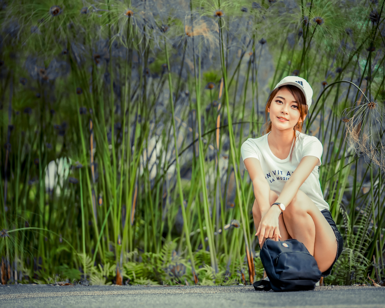 Милая девушка в кепке сидит на дороге с рюкзаком