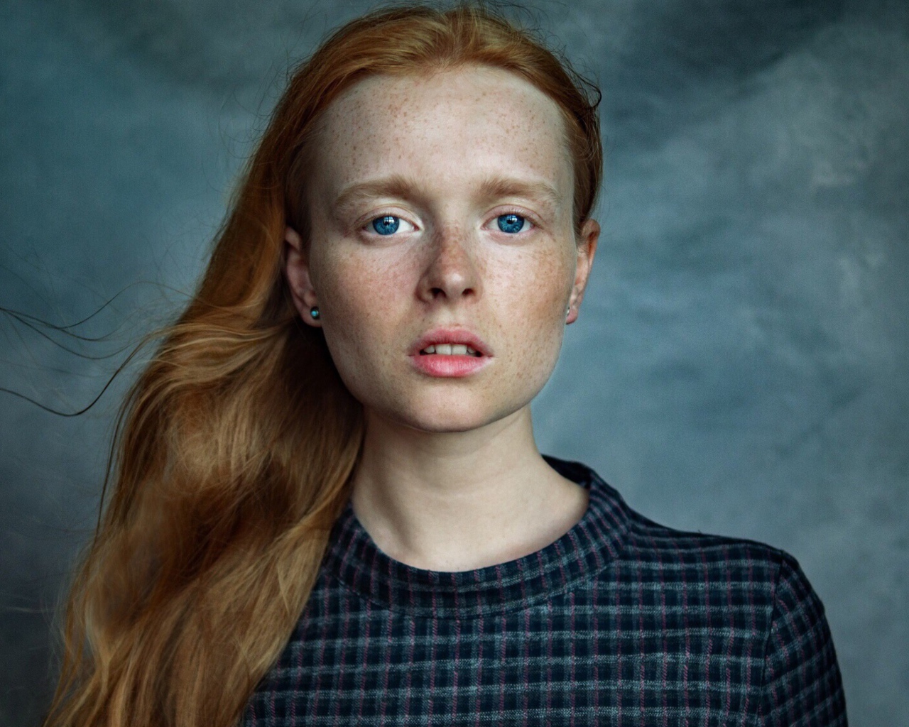 Милая рыжеволосая голубоглазая девушка с веснушками на лице на сером фоне