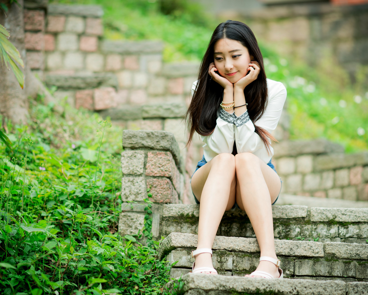 Мечтательная девушка азиатка сидит на ступеньках 