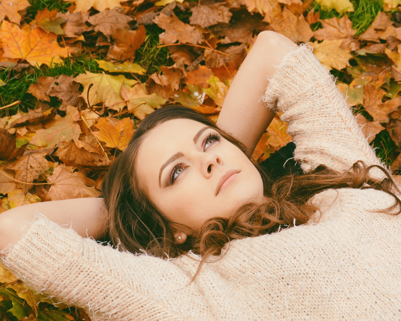 Мечтательная девушка в свитере лежит на земле