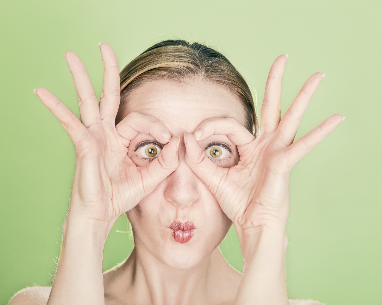 Смешная девушка делает руками очки на лице