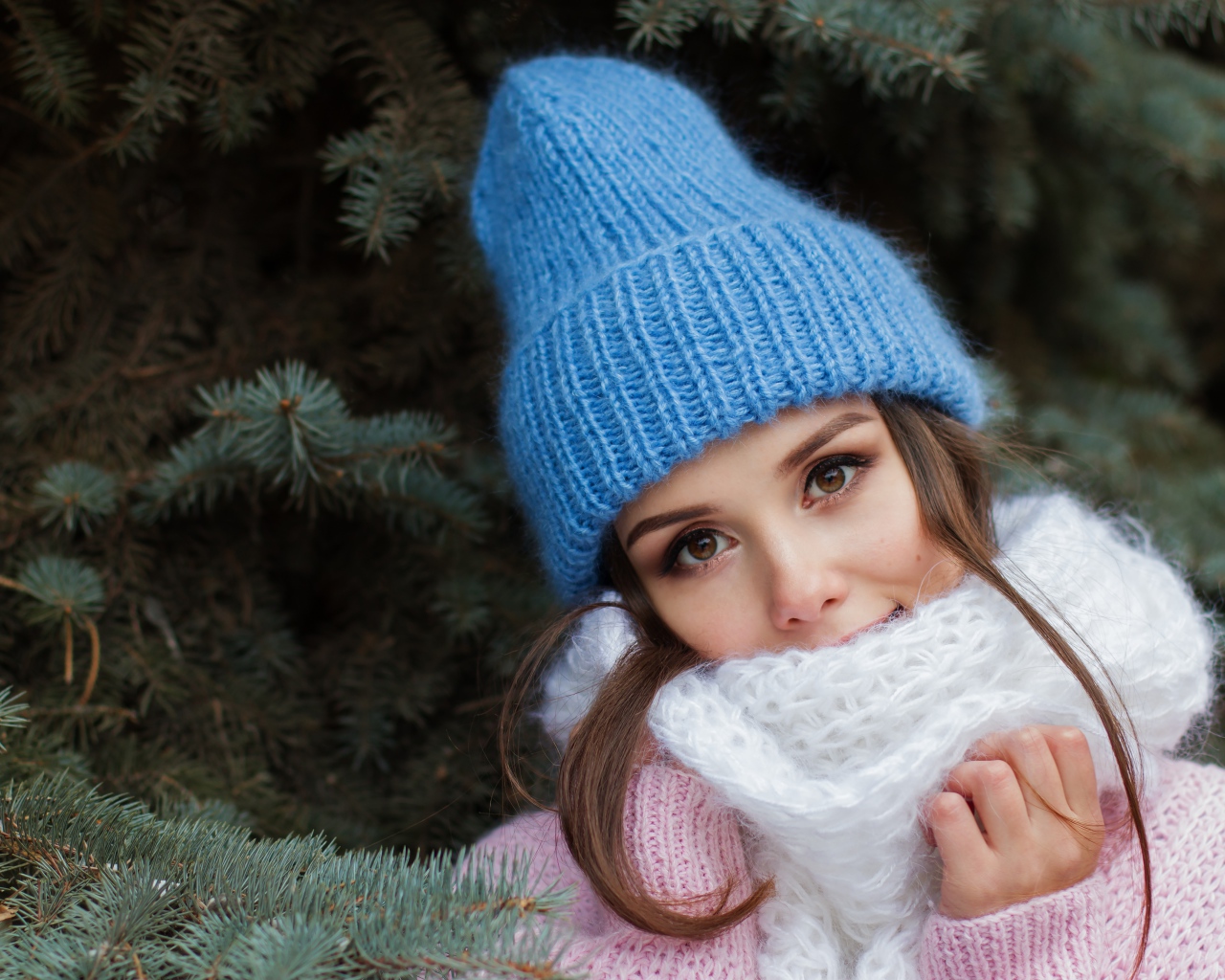 Девушка в голубой вязаной шапке у ели