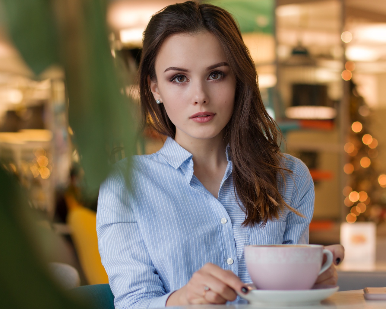 Девушка в голубой рубашке с чашкой кофе на столе в кафе