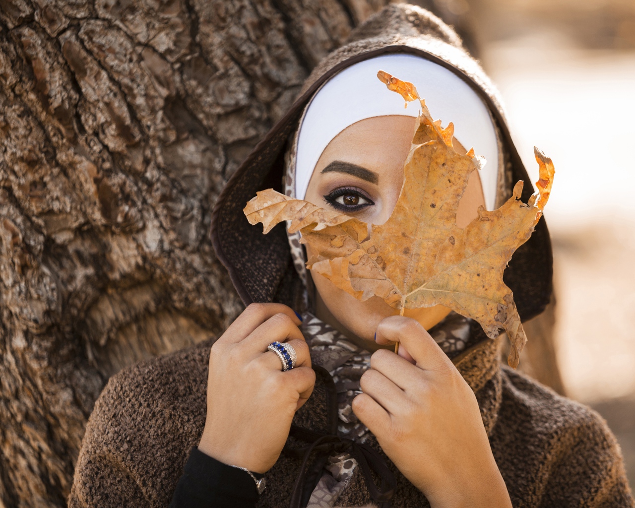 Девушка в пальто с закрывает лицо листом