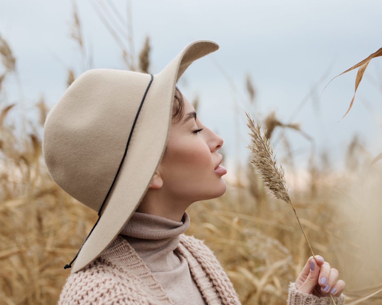 Девушка в шляпе с закрытыми глазами держит колосок 