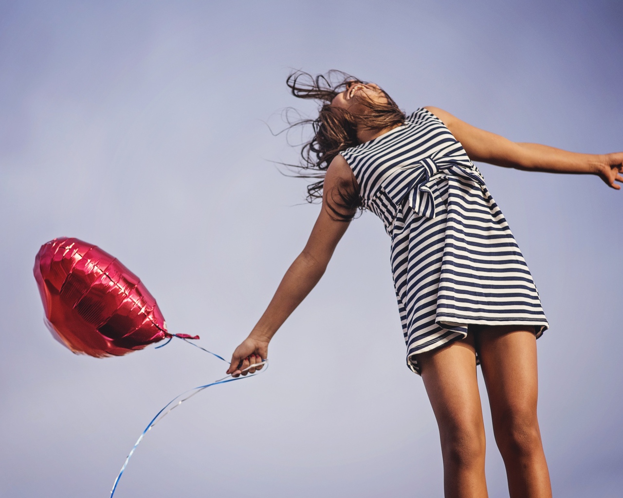 Девушка в полосатом платье прыгает с шариком 