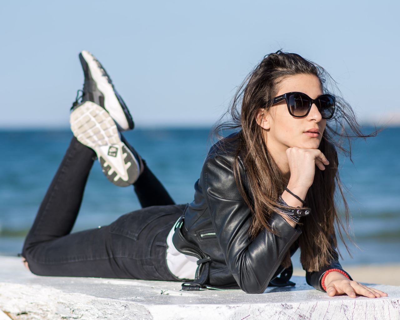 Девушка в черных очках и кожаной куртке на фоне моря