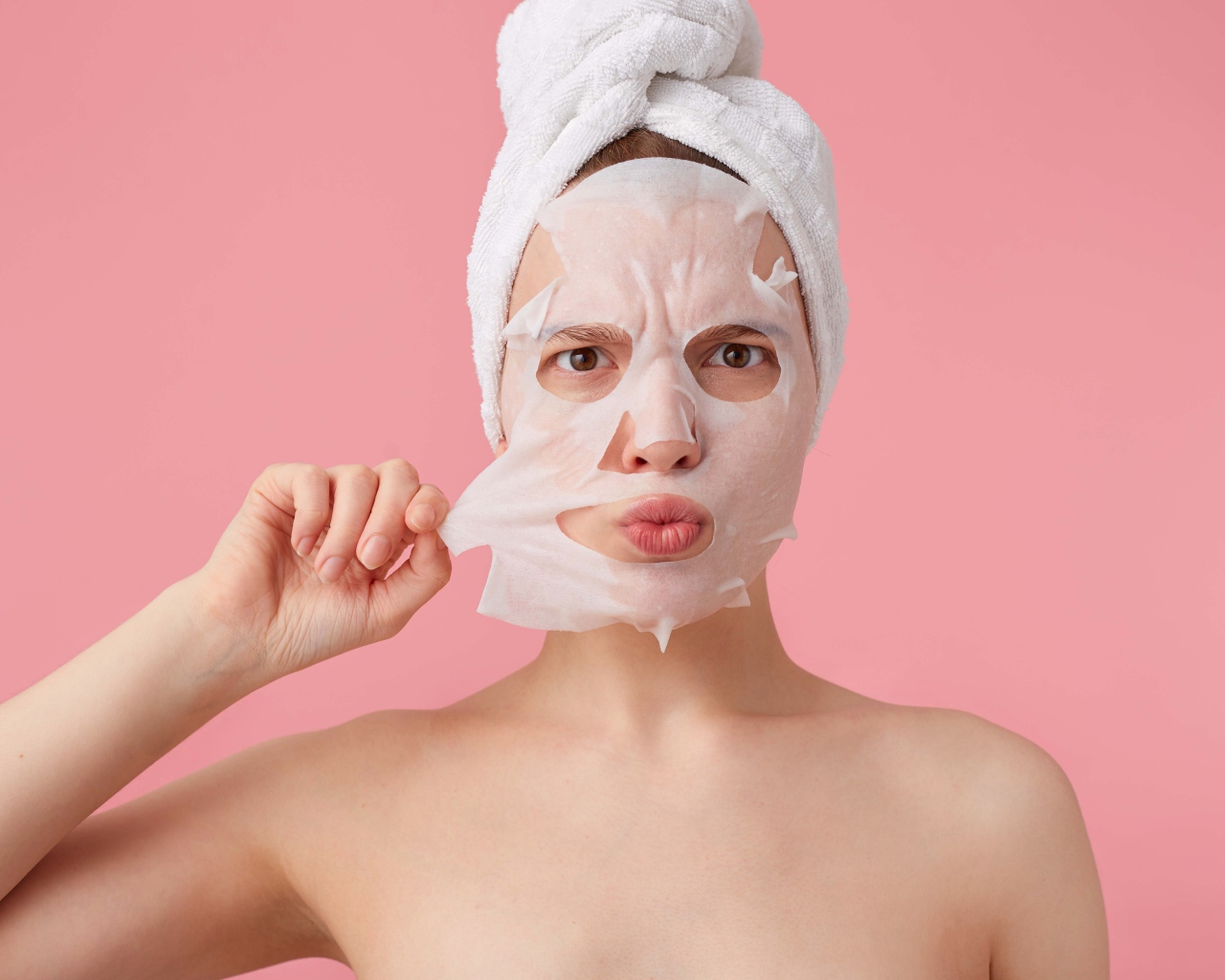 Девушка снимает косметическую маску с лица на розовом фоне 