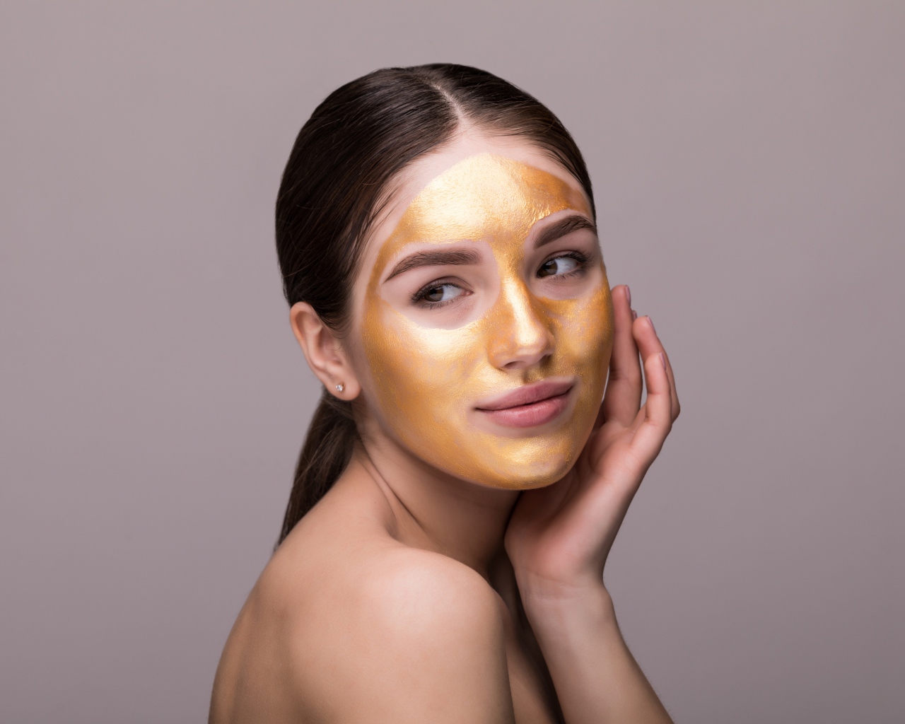 Золотая маска на лице у молодой девушки 