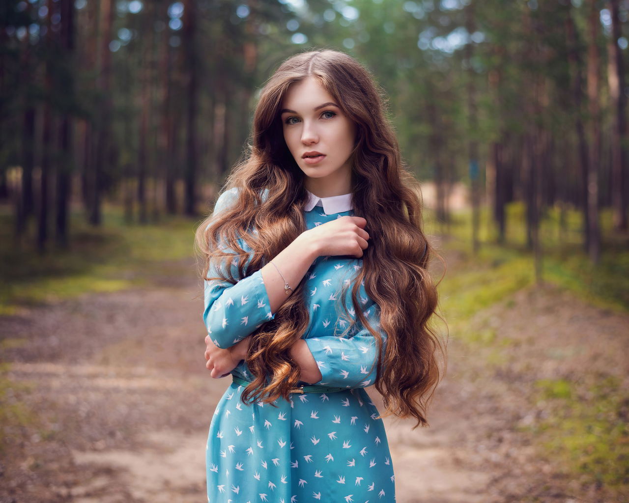 Длинноволосая девушка в голубом платье стоит в лесу