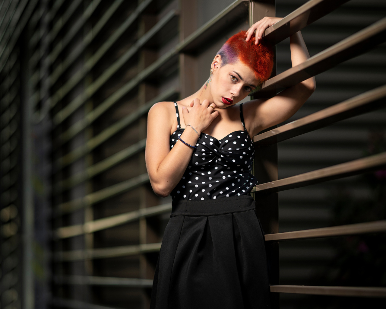 Эпатажная девушка с короткой стрижкой стоит у забора 