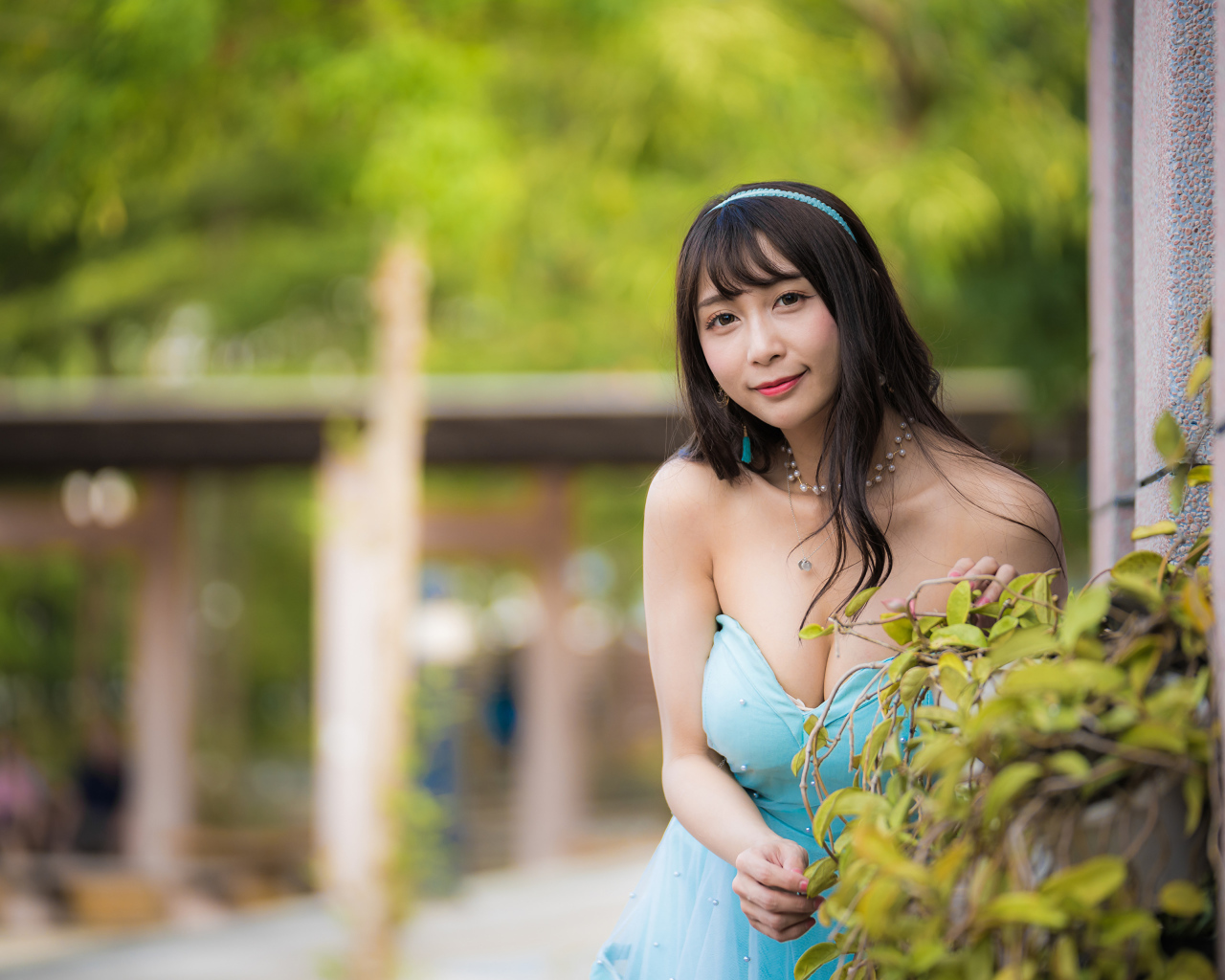 Улыбающаяся девушка азиатка в голубом платье у стены с растением 
