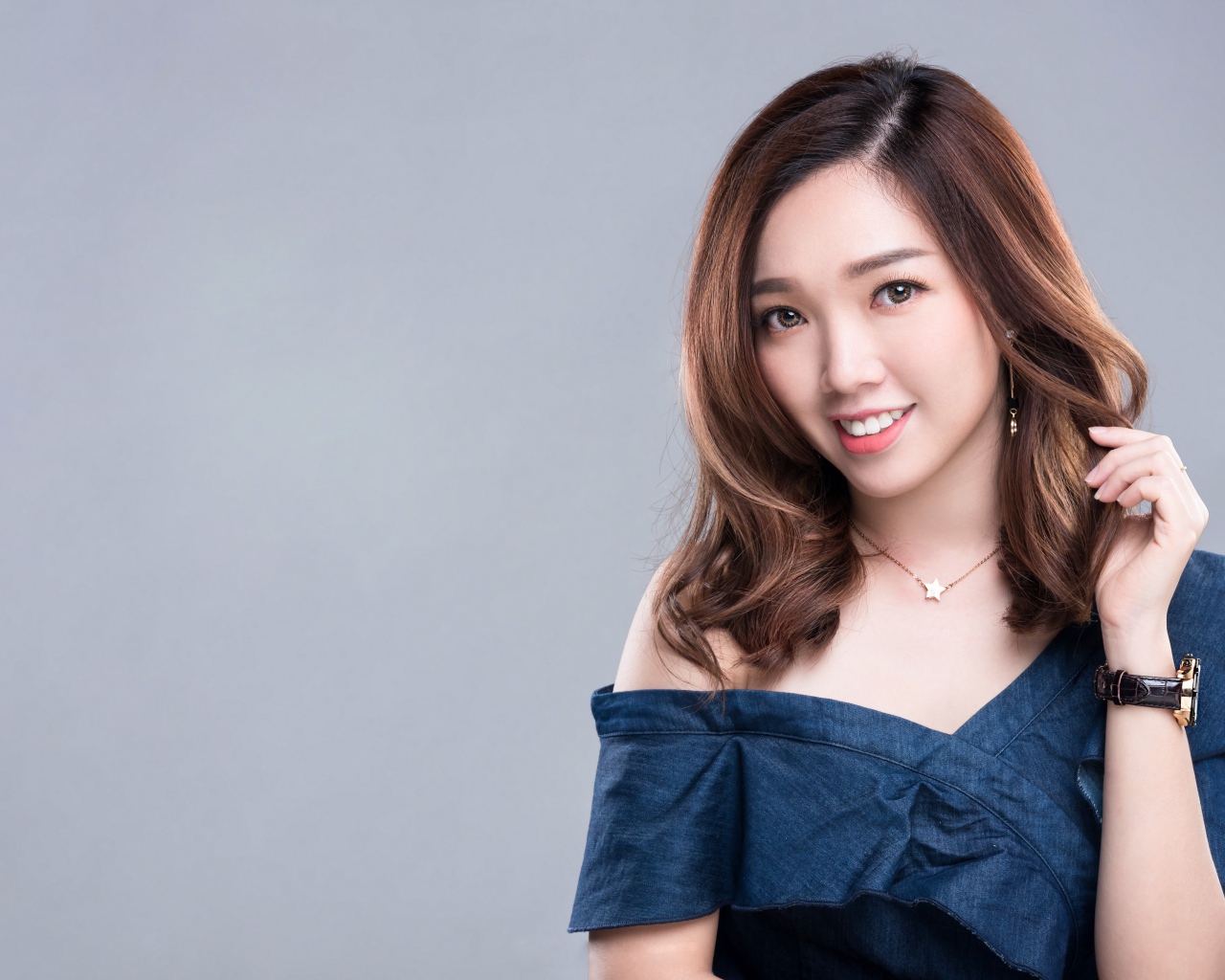 Улыбающаяся девушка азиатка с часами на руке на сером фоне