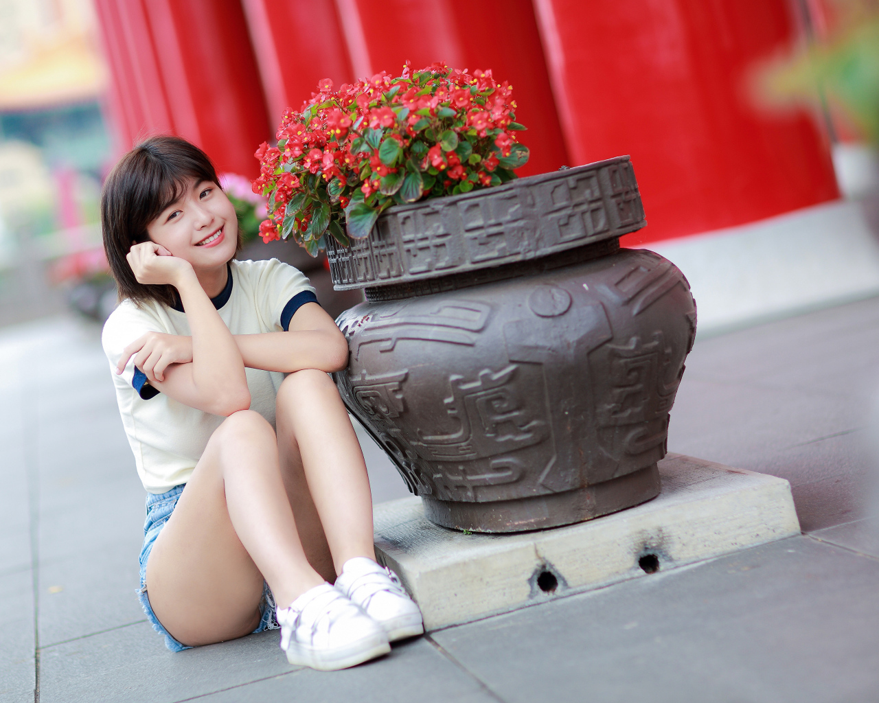 Улыбающаяся азиатка сидит у клумбы с цветами