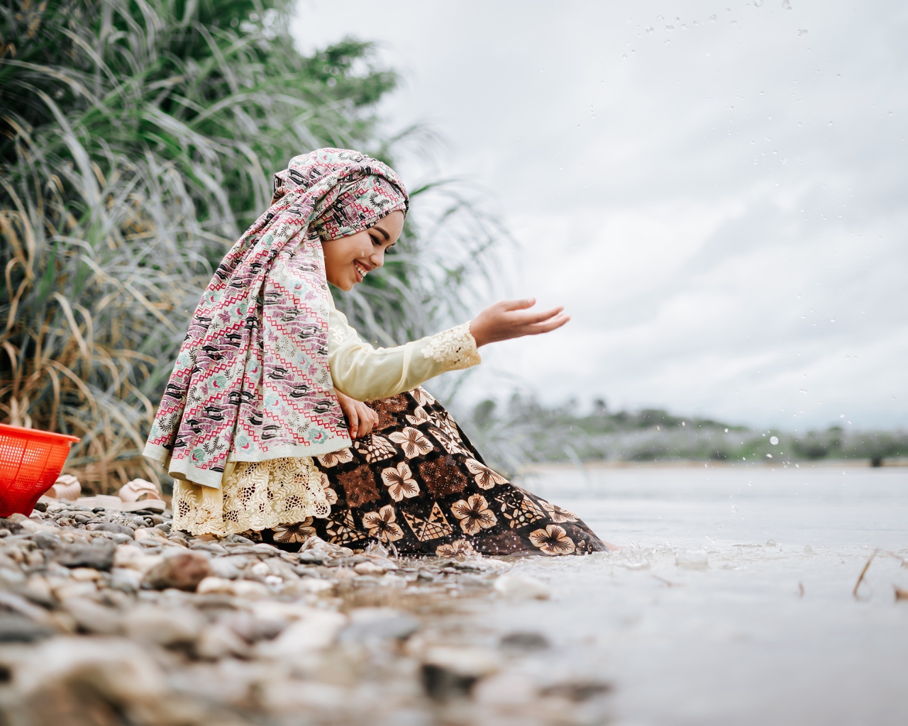Улыбающаяся девушка азиатка сидит у воды