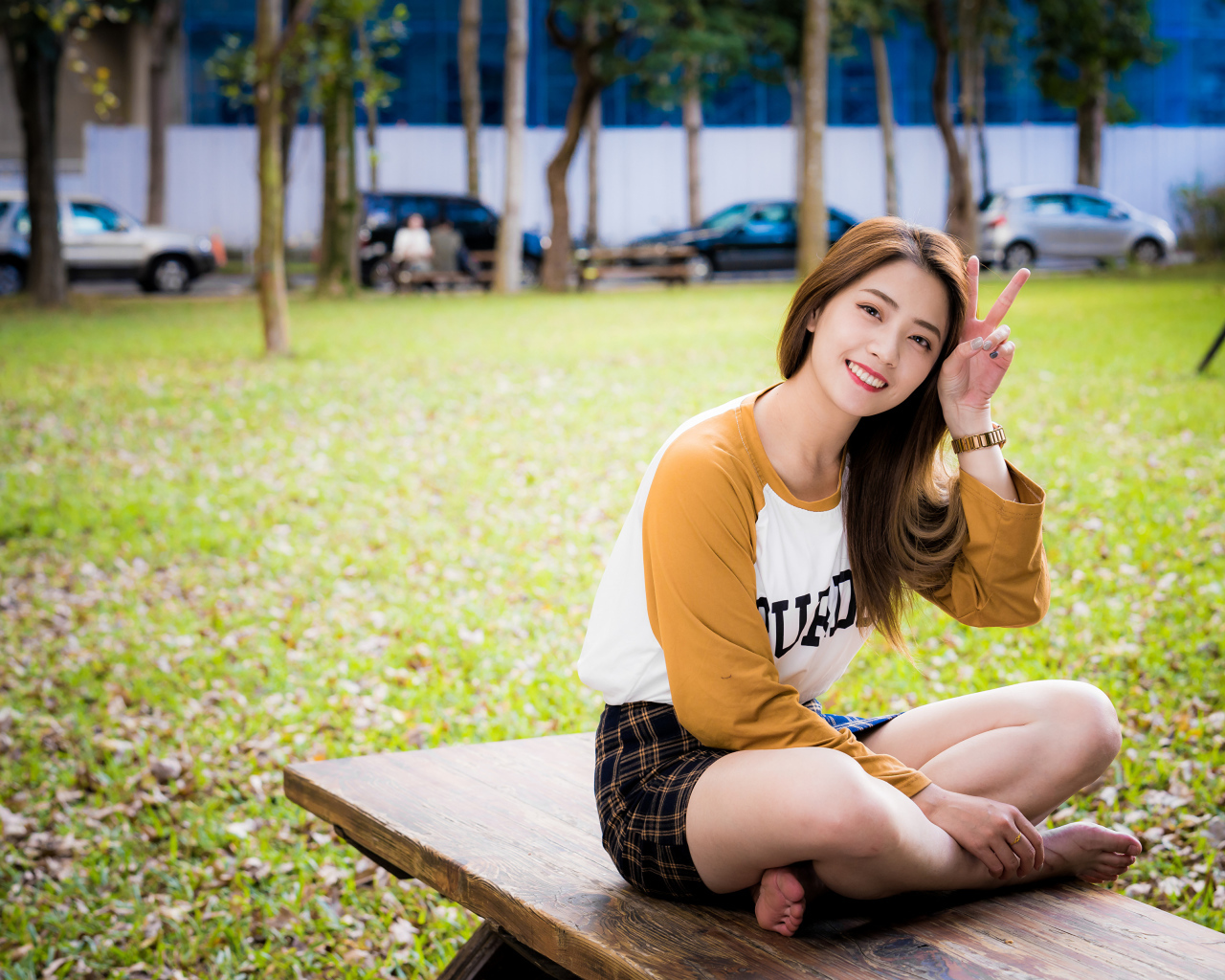 Улыбающаяся девушка азиатка сидит на лавке в парке 