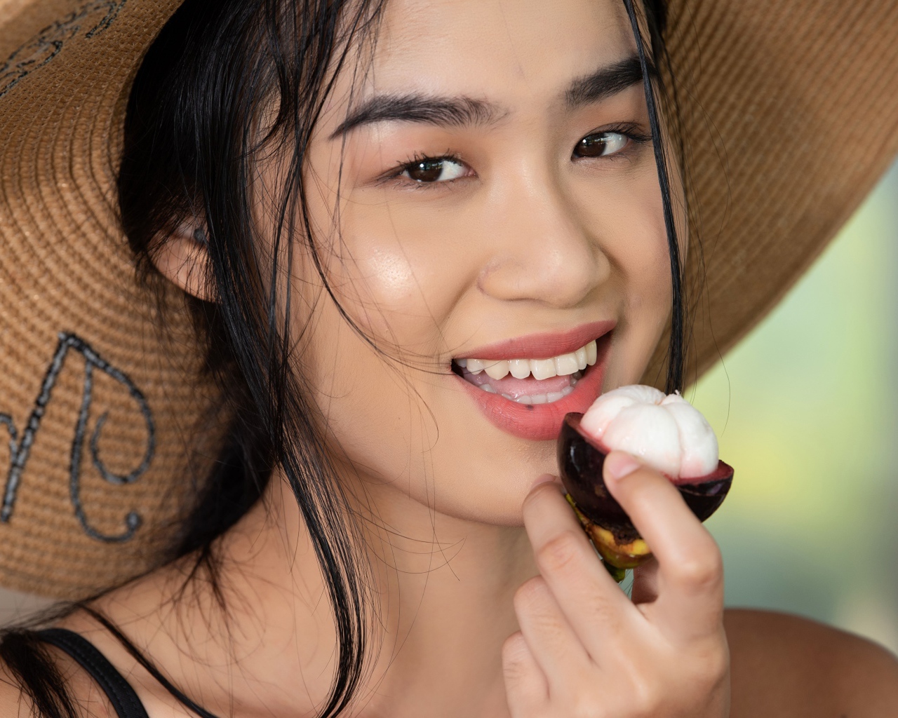 Улыбающаяся азиатка в шляпе с фруктом в руке