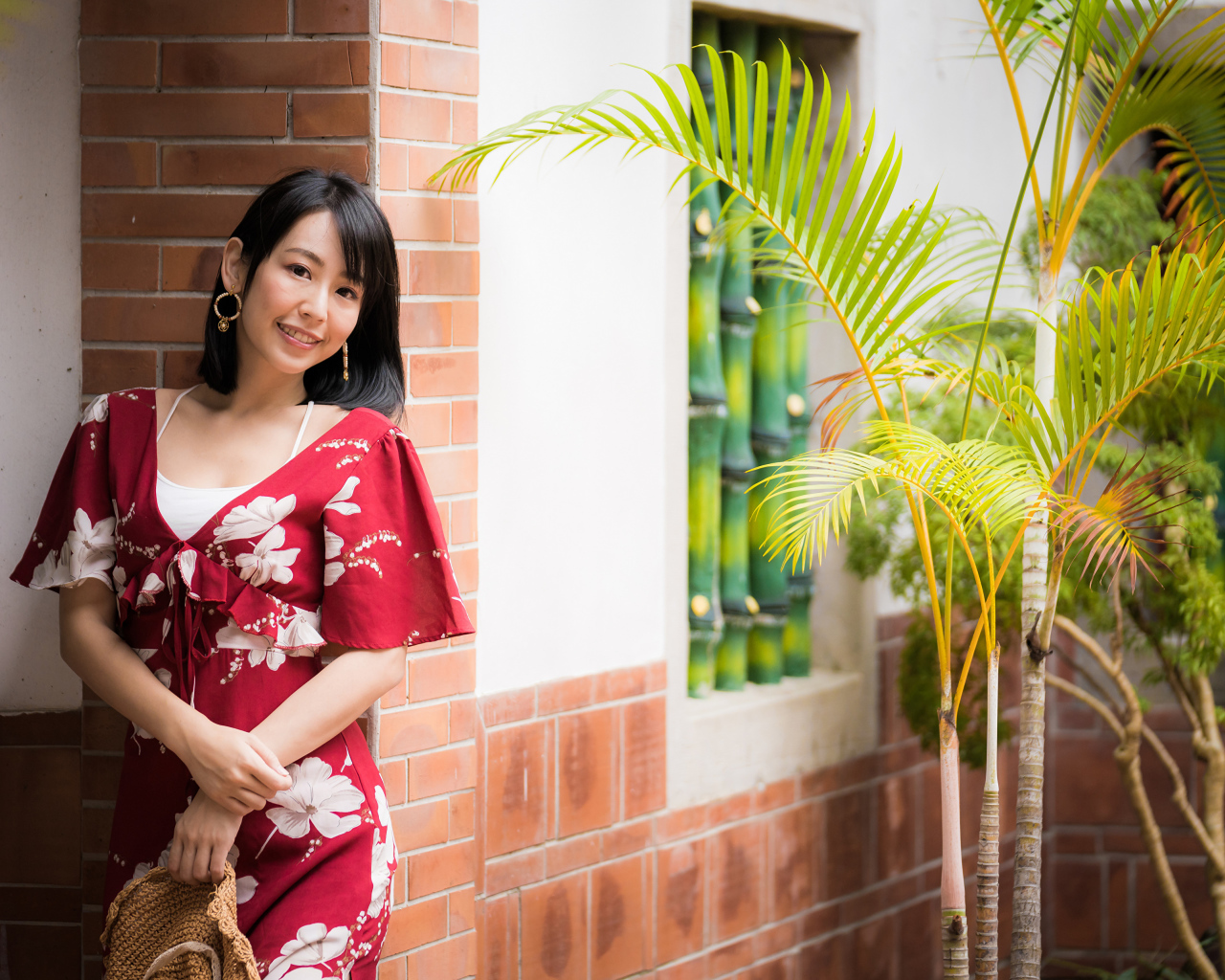 Улыбающаяся азиатка в красном платье стоит у стены 