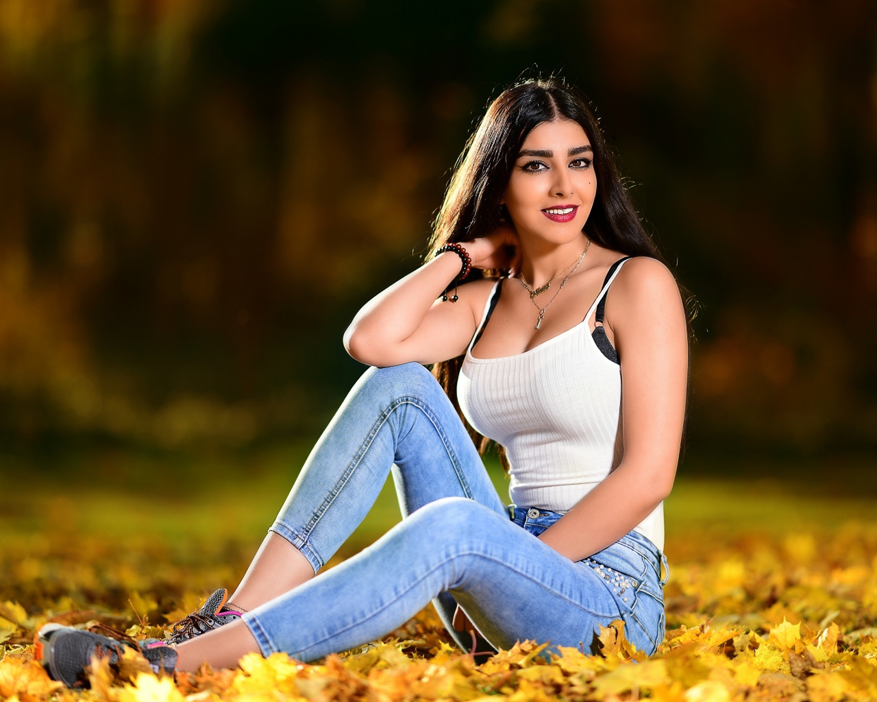Улыбающаяся брюнетка сидит на опавшей листве