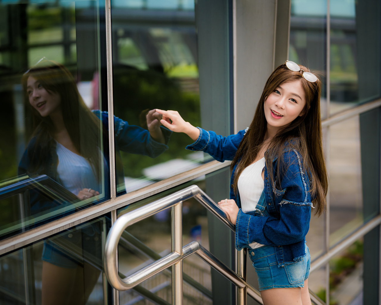 Улыбающаяся девушка в джинсовой куртке стоит у стены 