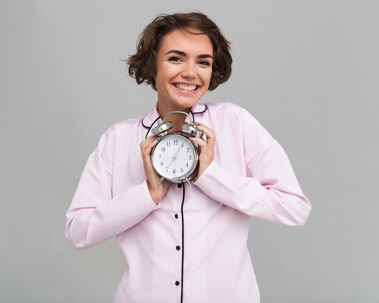 Улыбающаяся девушка в пижаме держит будильник 