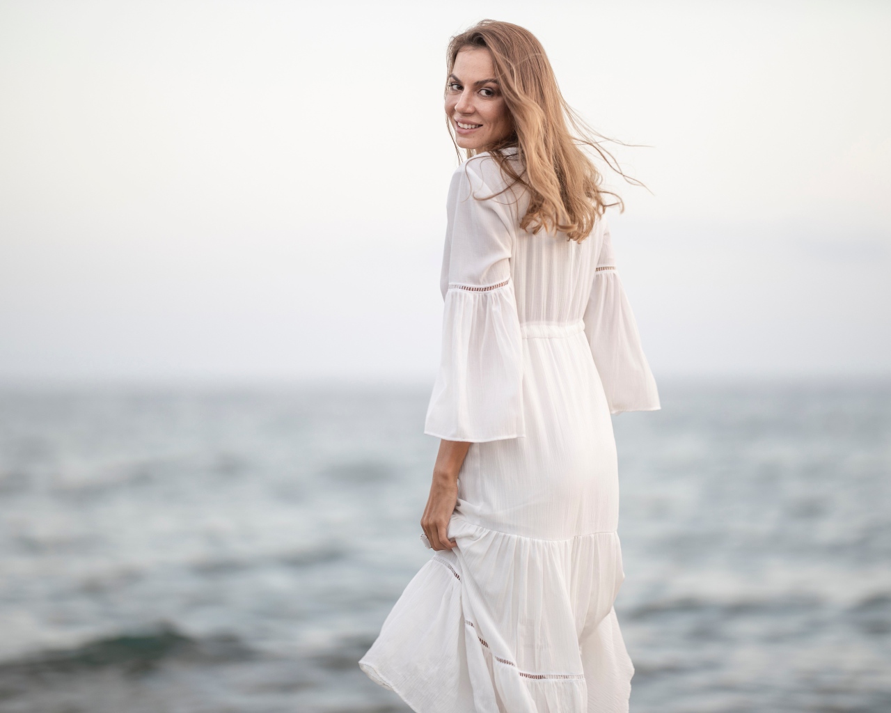 Улыбающаяся девушка в белом платье на фоне моря