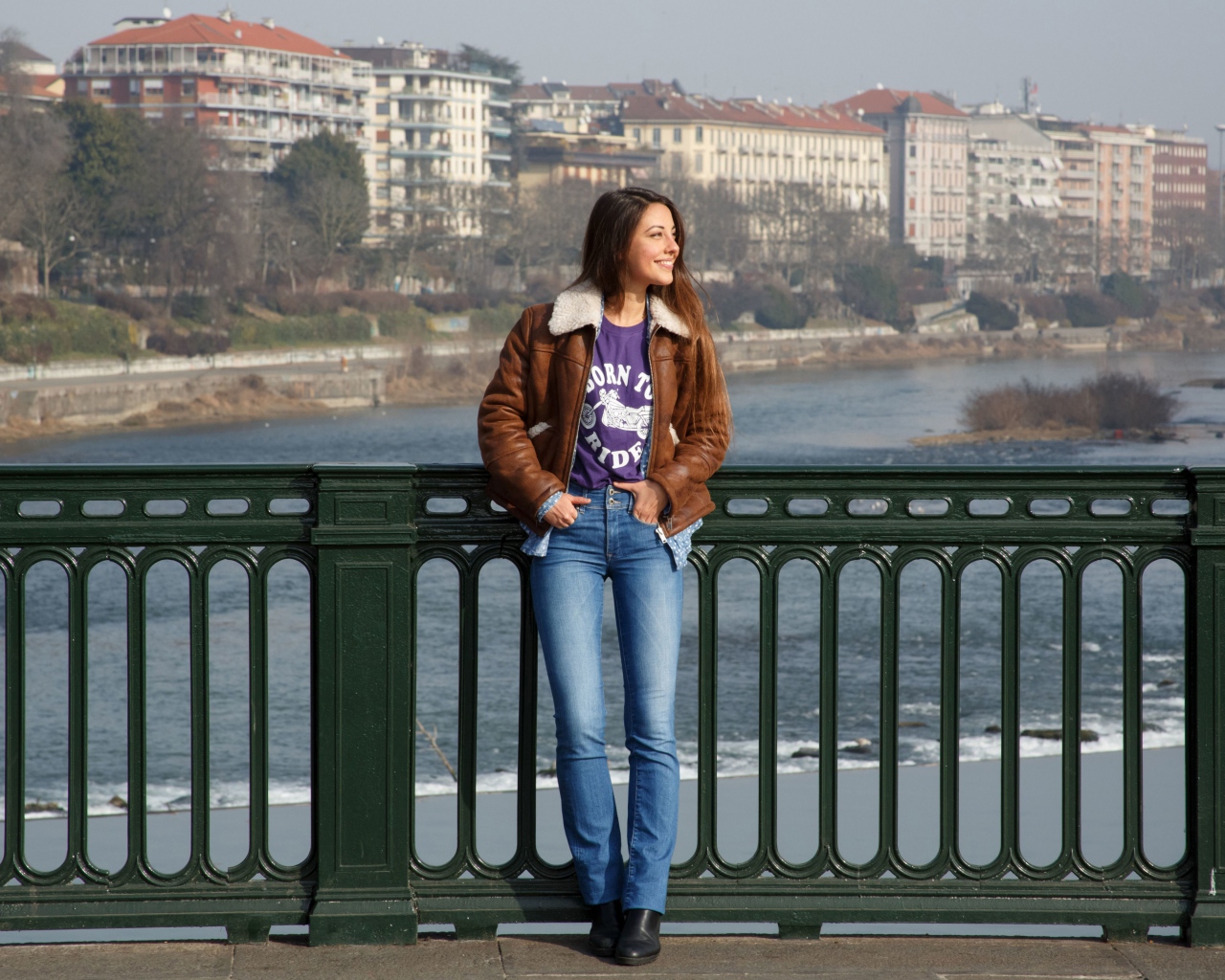 Улыбающаяся девушка стоит на мосту у реки