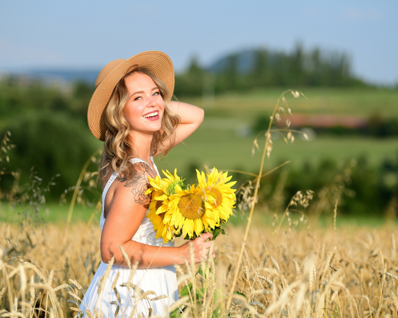Улыбающаяся девушка с букетом подсолнухов на поле пшеницы