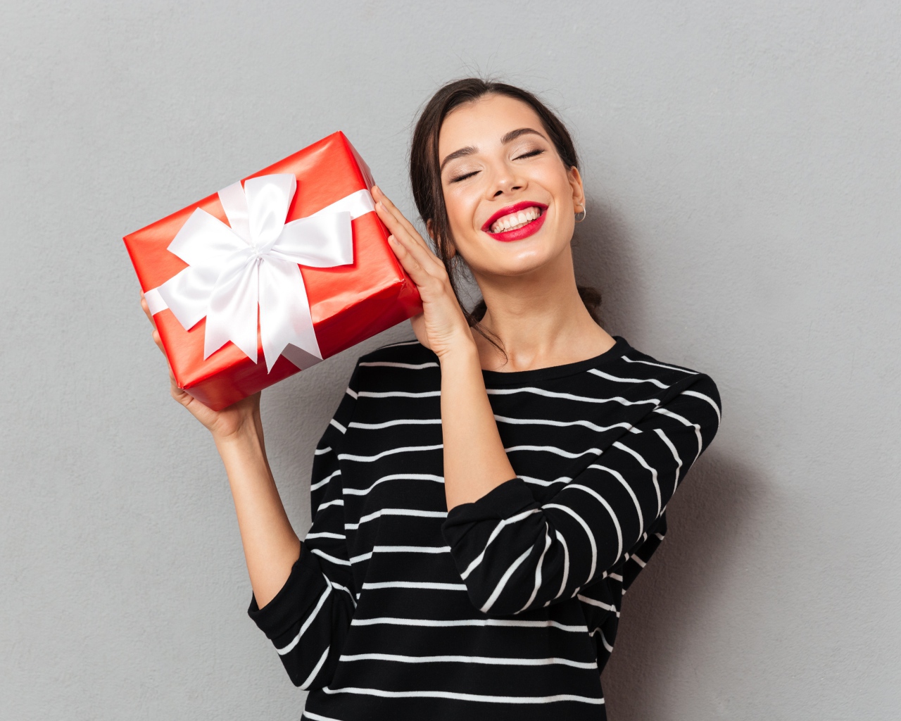 Улыбающаяся девушка с подарком в руках на сером фоне 