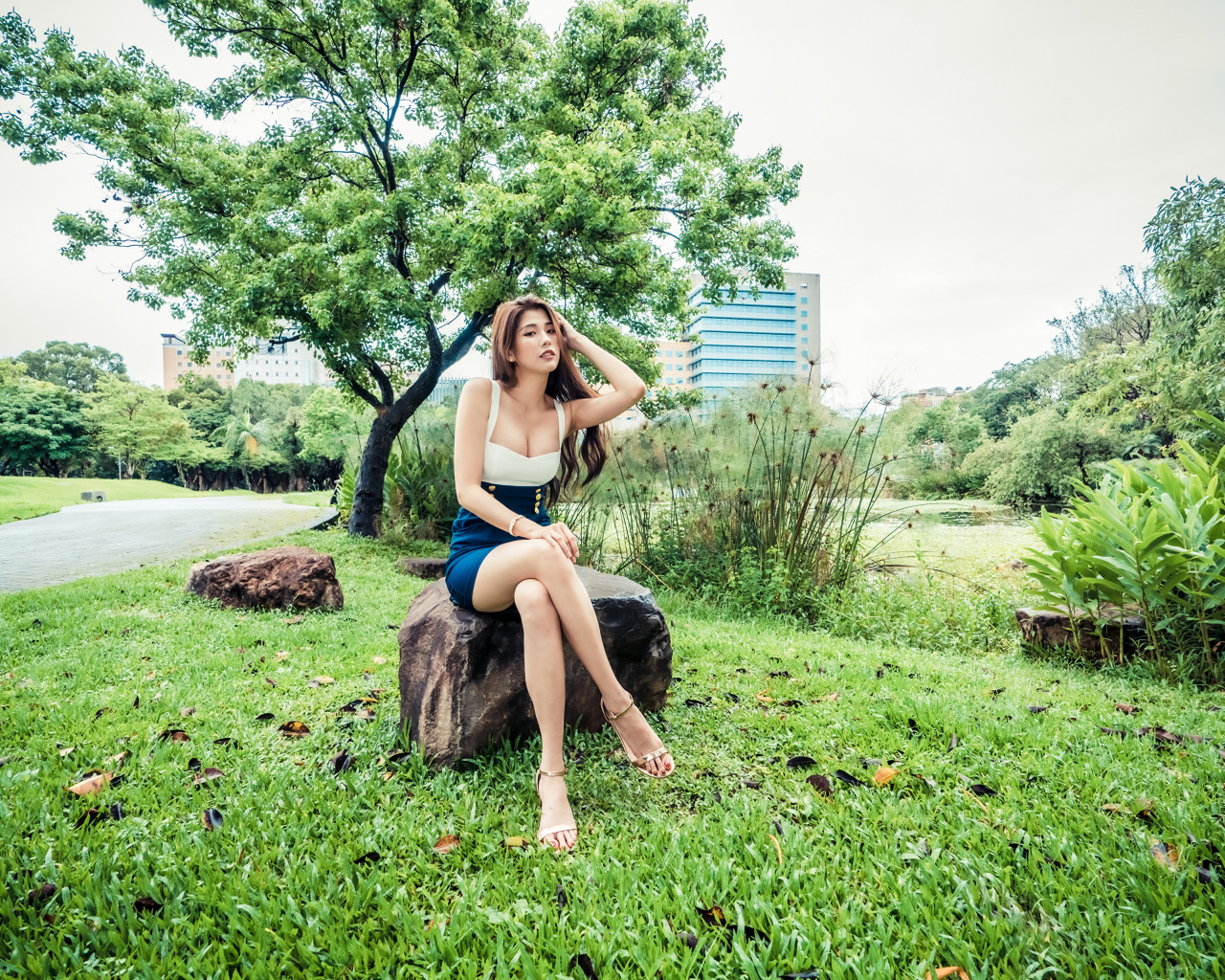Эффектная девушка азиатка сидит на камне в парке