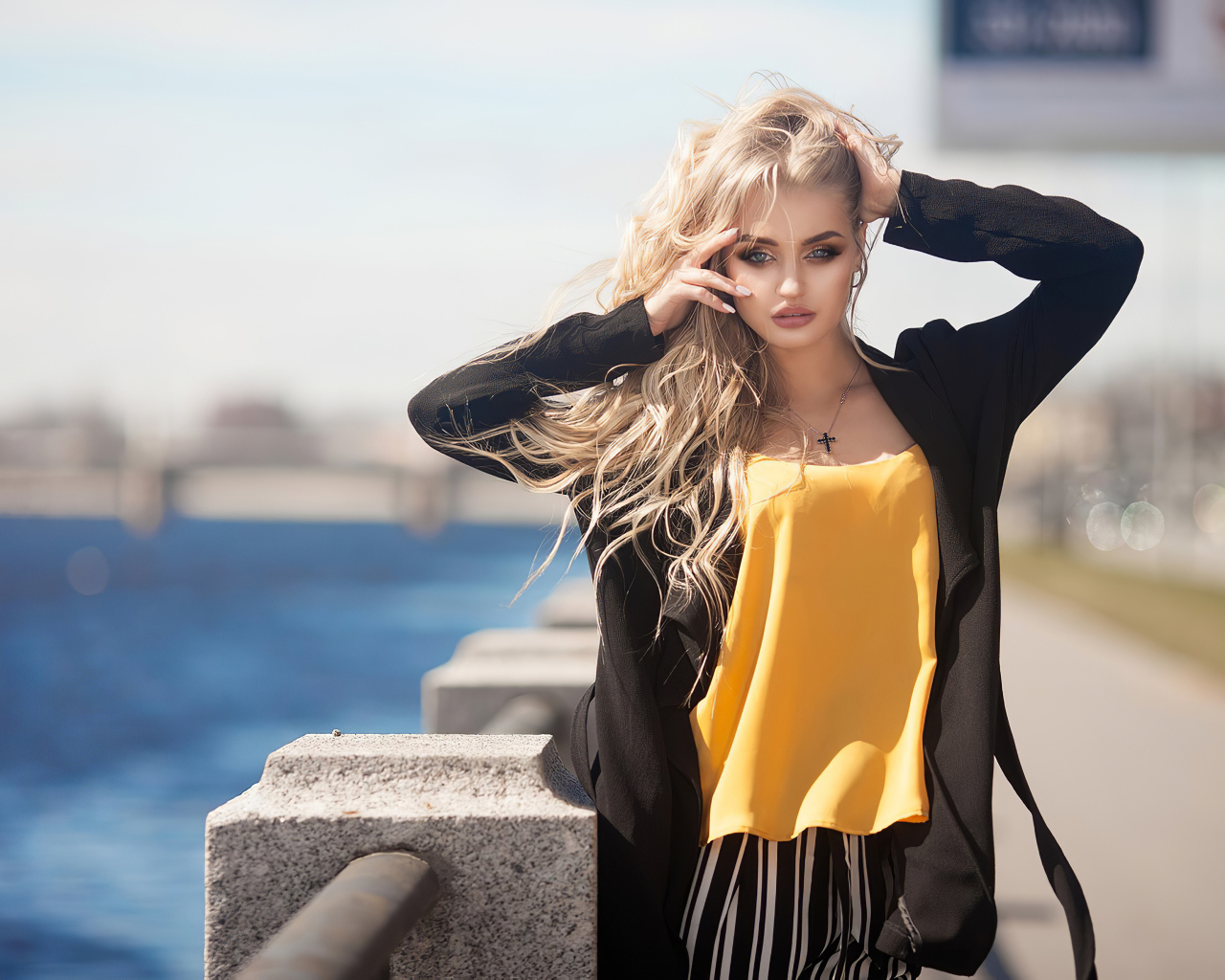 Эффектная блондинка в черном пальто стоит у воды