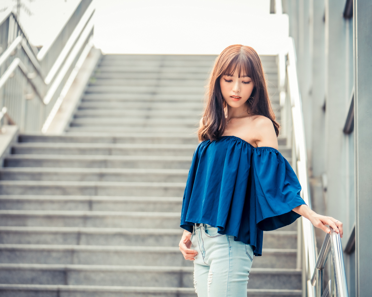 Стильная девушка азиатка с опущенной головой стоит на ступеньках 