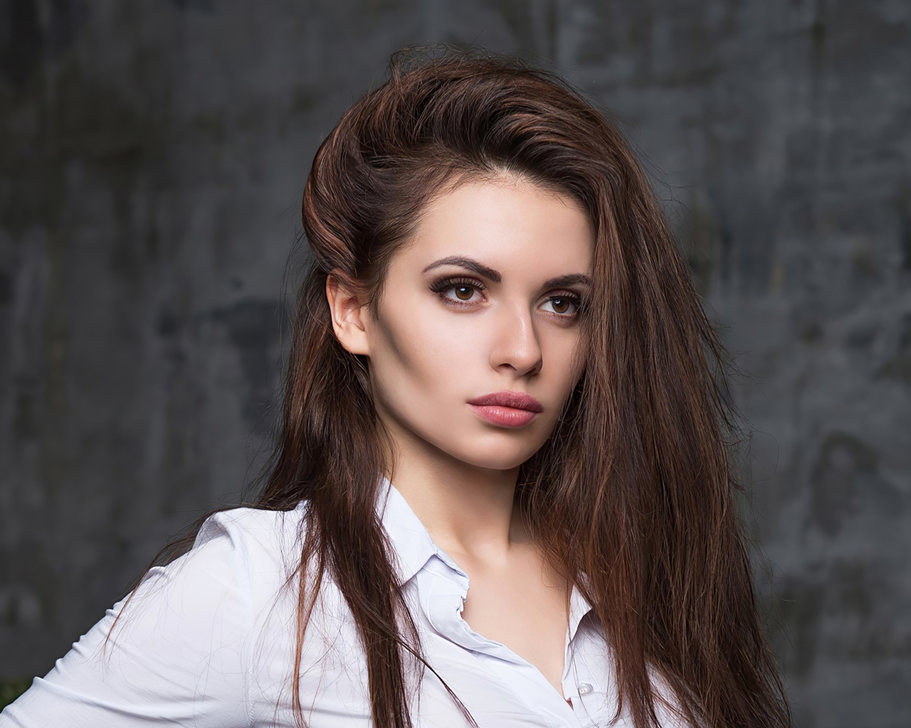 Стильная девушка в белой рубашке на фоне серой стены 
