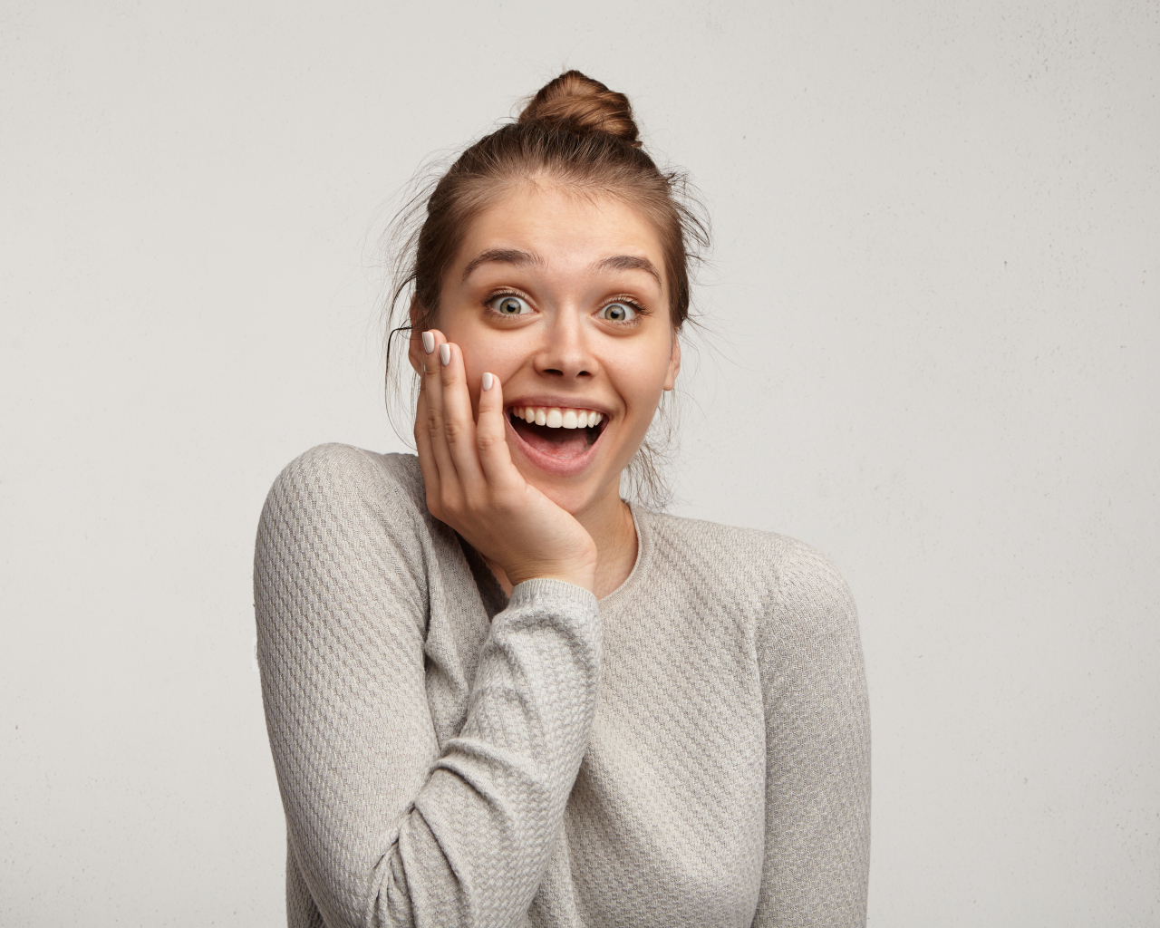 Удивленная девушка с рукой у лица на сером фоне 