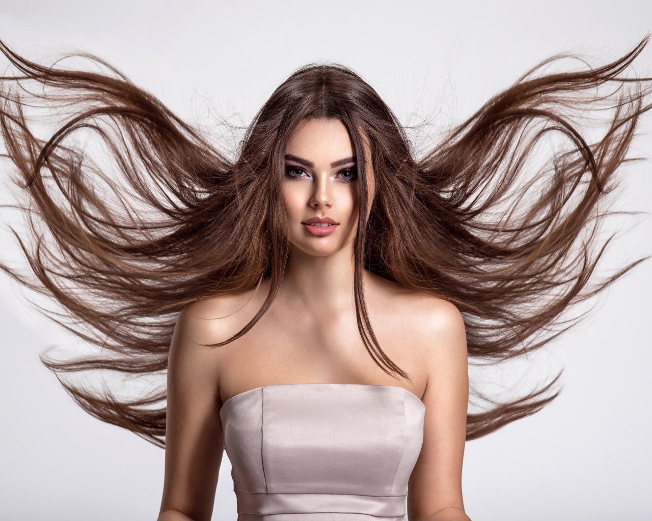 Ветер развивает волосы красивой девушке шатенке на сером фоне