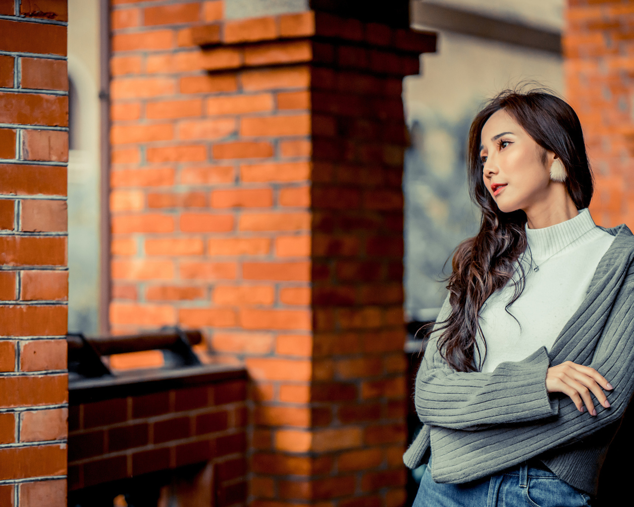 Молодая девушка азиатка в серой кофте у кирпичной стены 