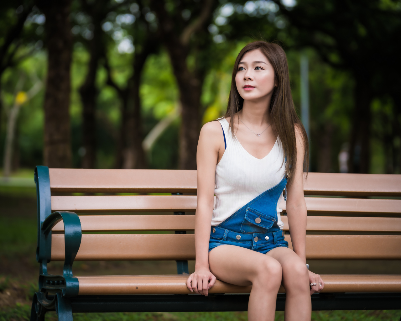 Молодая девушка азиатка сидит в парке на лавочке