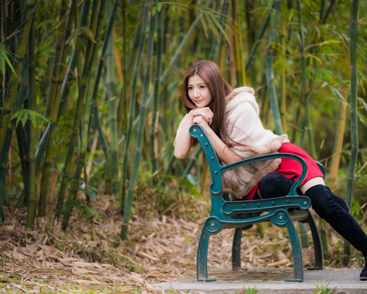 Молодая девушка азиатка сидит на зеленой лавке 