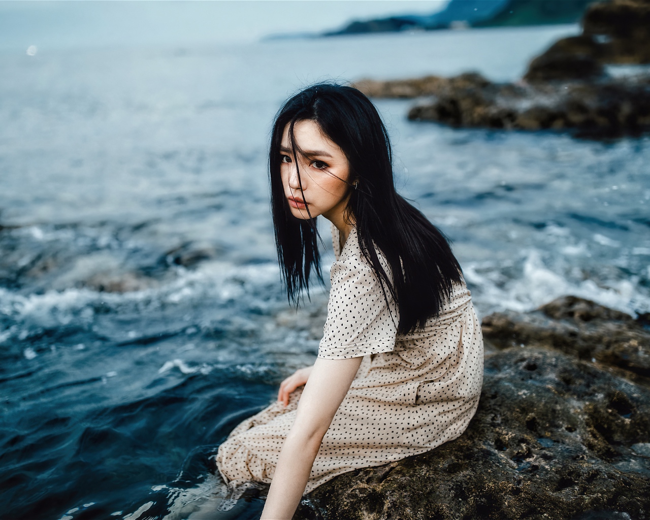 Молодая девушка азиатка сидит на камне у воды
