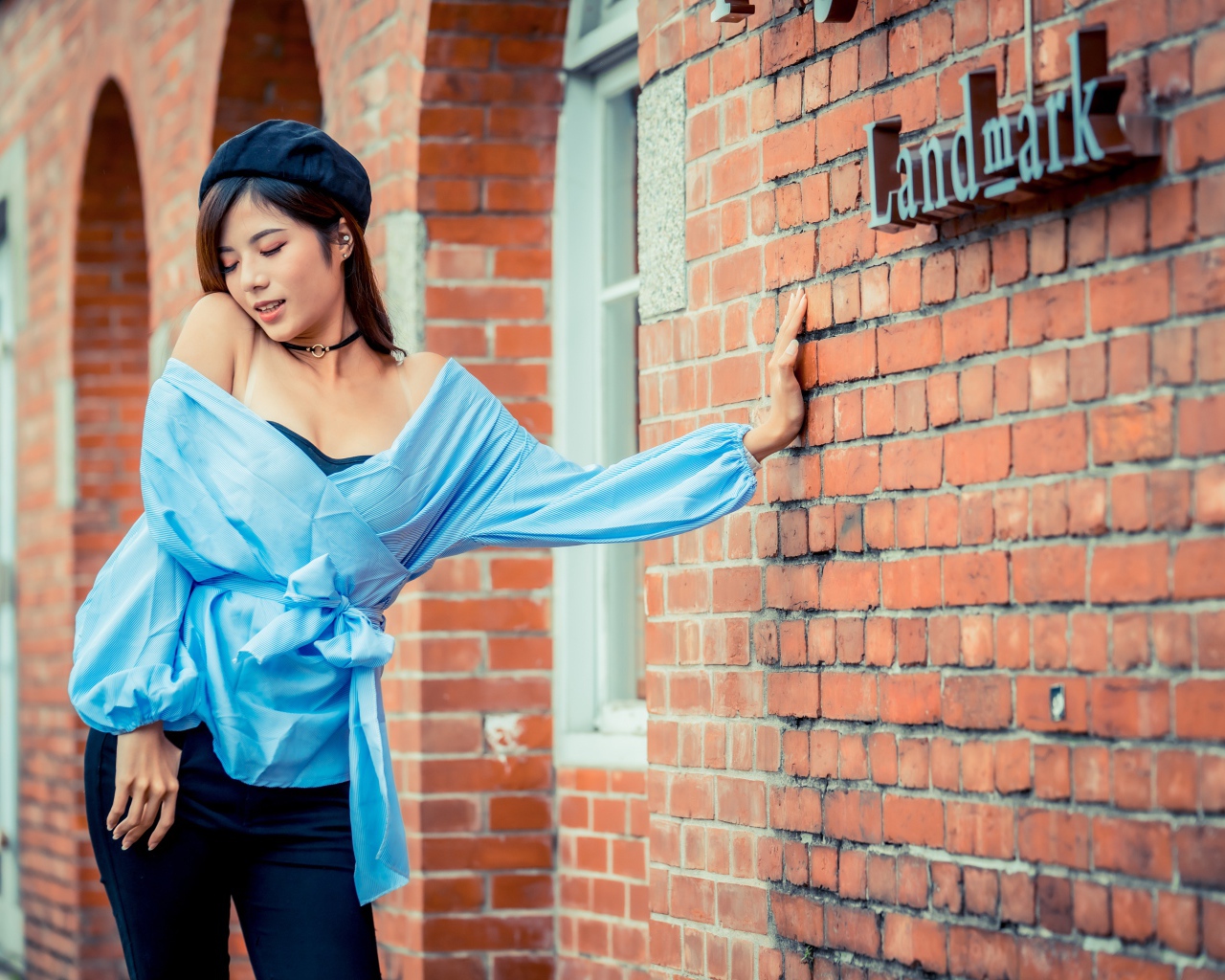 Молодая азиатка в черном берете стоит у стены 