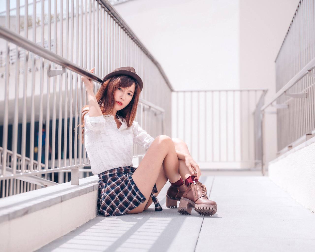 Молодая азиатка в короткой юбке сидит у перил 