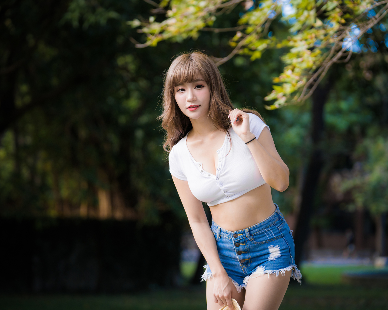 Молодая азиатка в белом топе и синих шортах  в парке