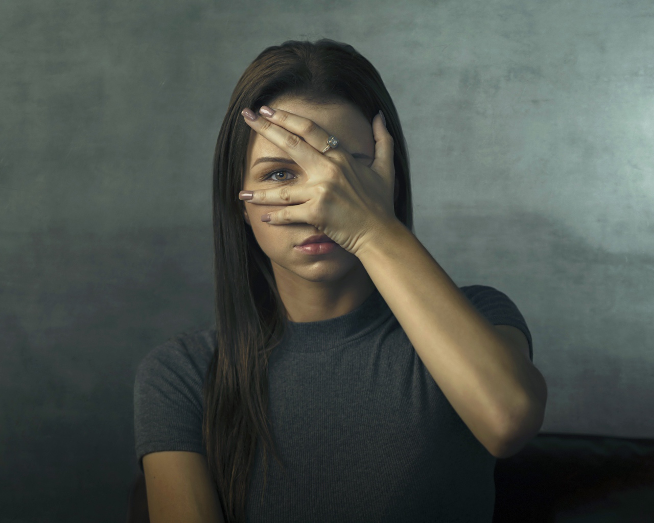 Молодая девушка закрыла лицо рукой на сером фоне