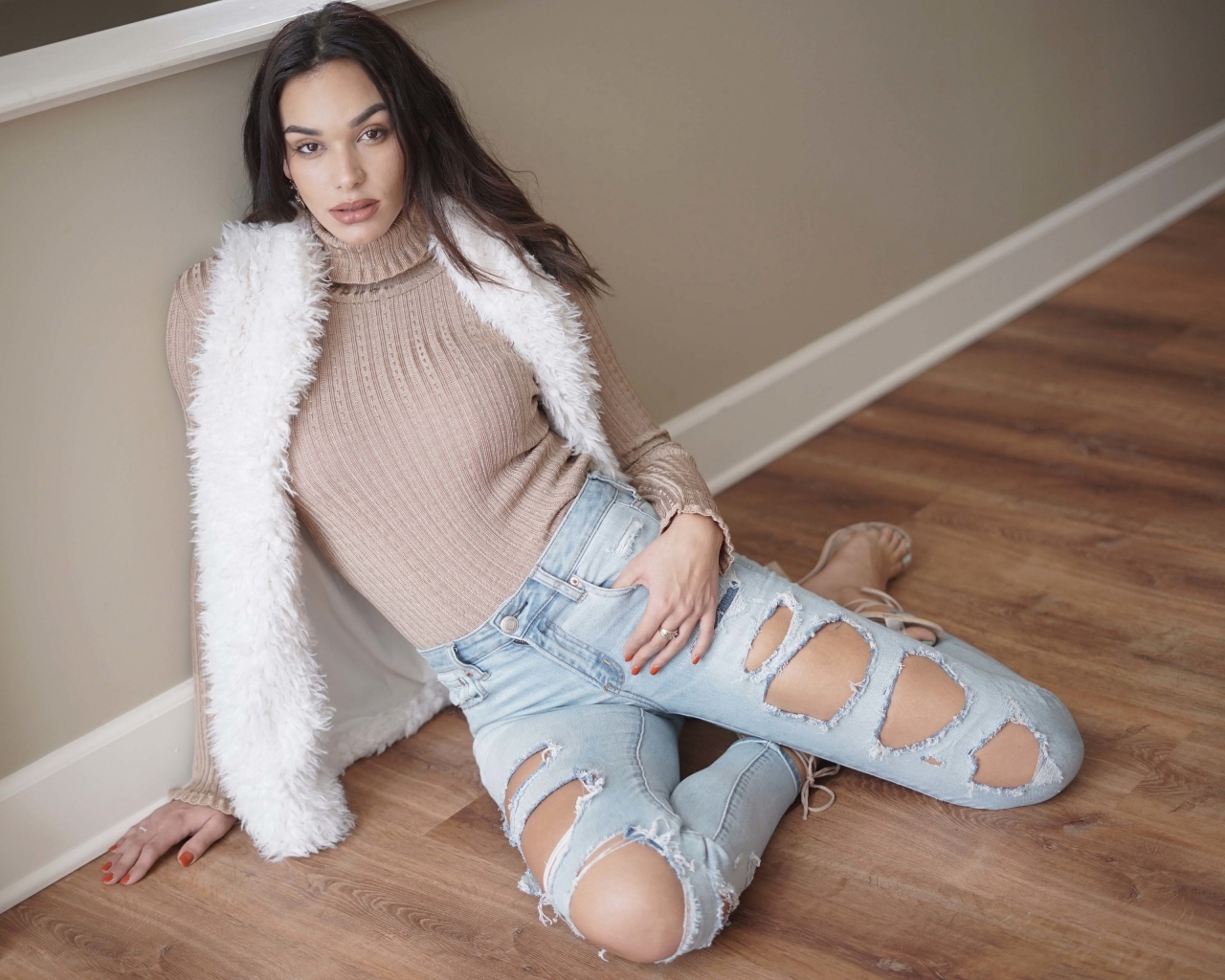 Молодая девушка в рваных джинсах сидит у стены