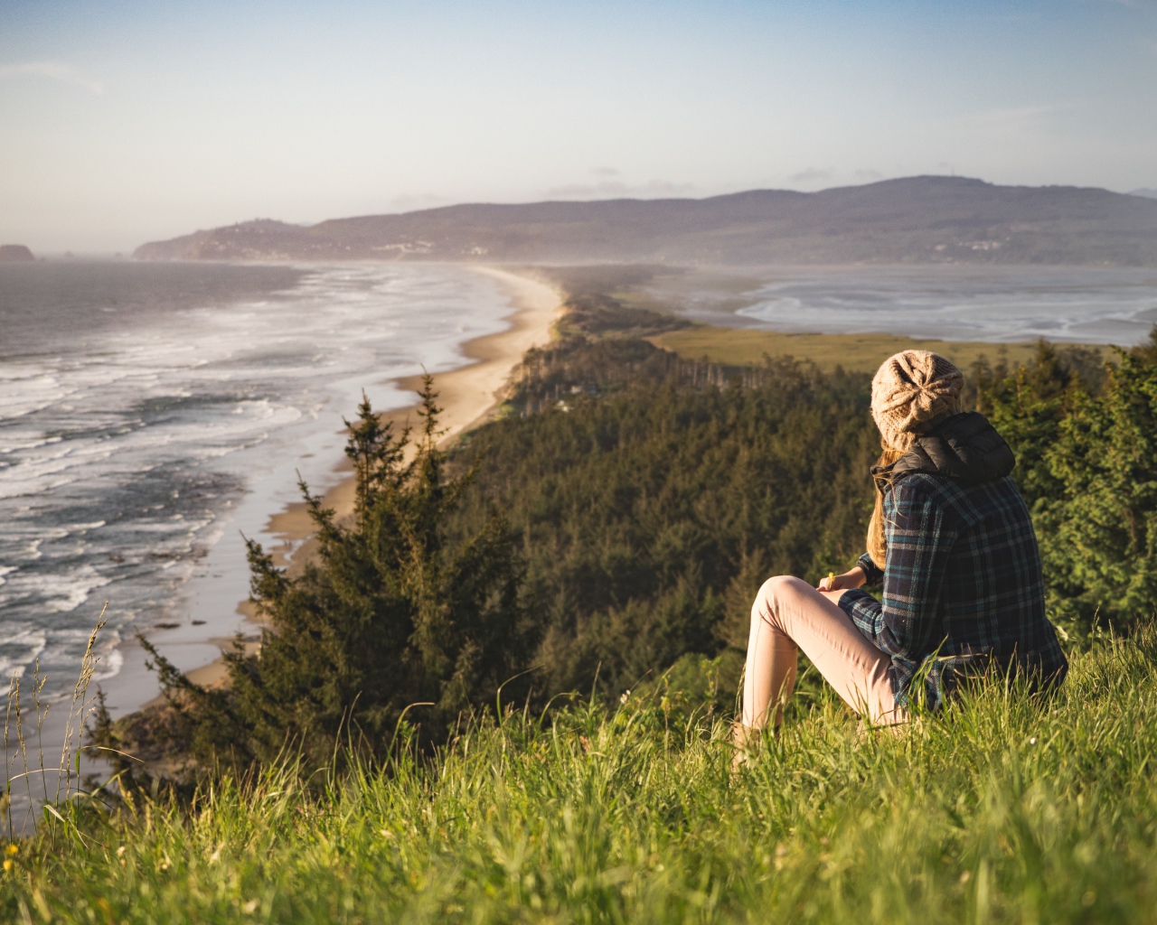 Молодая девушка сидит на зеленой траве на фоне моря