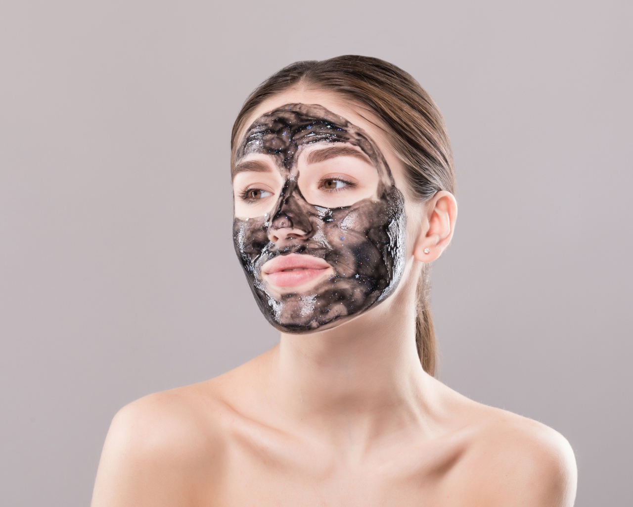 Молодая девушка с косметической черной маской на лице