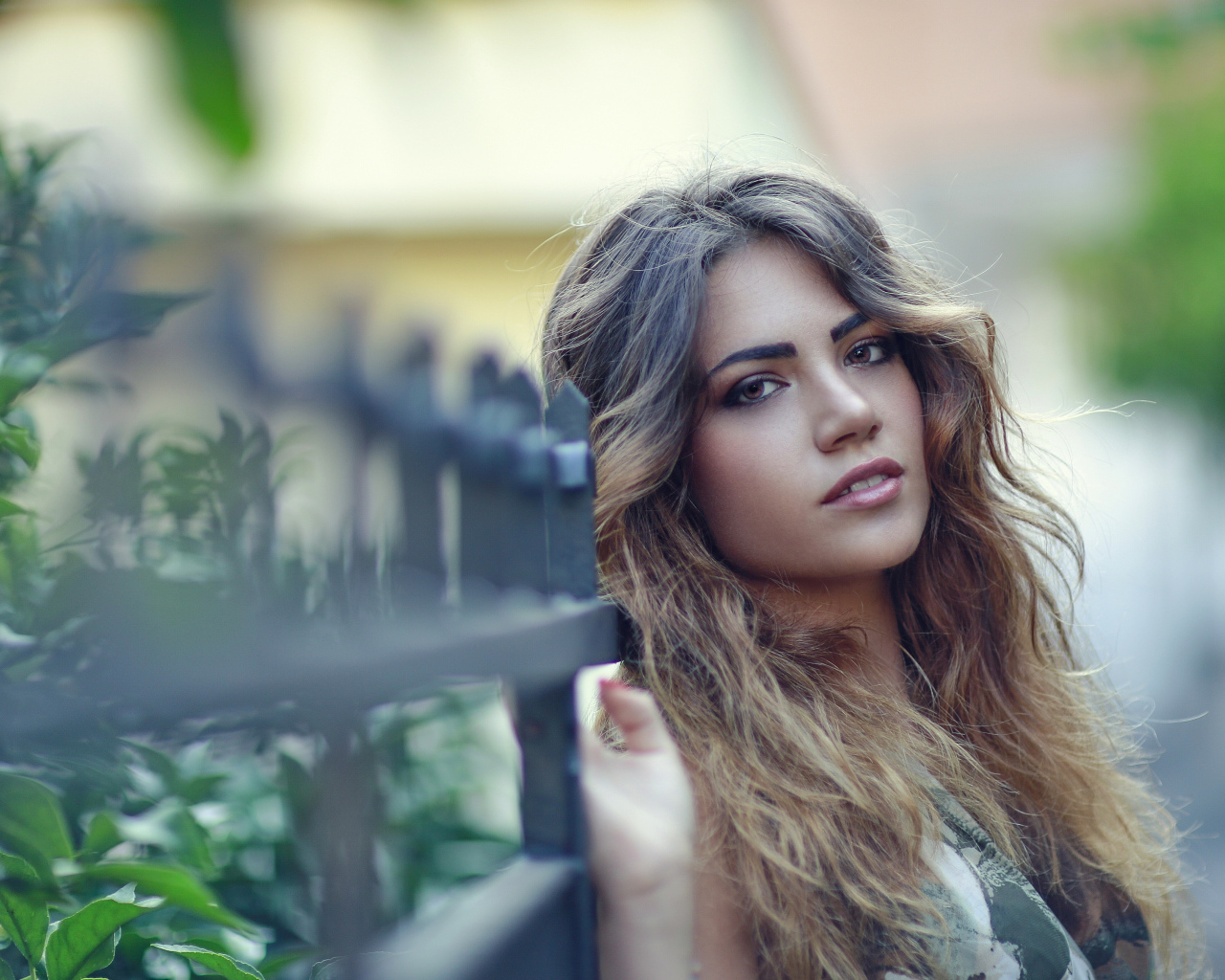 Молодая девушка с длинными волосами стоит у забора